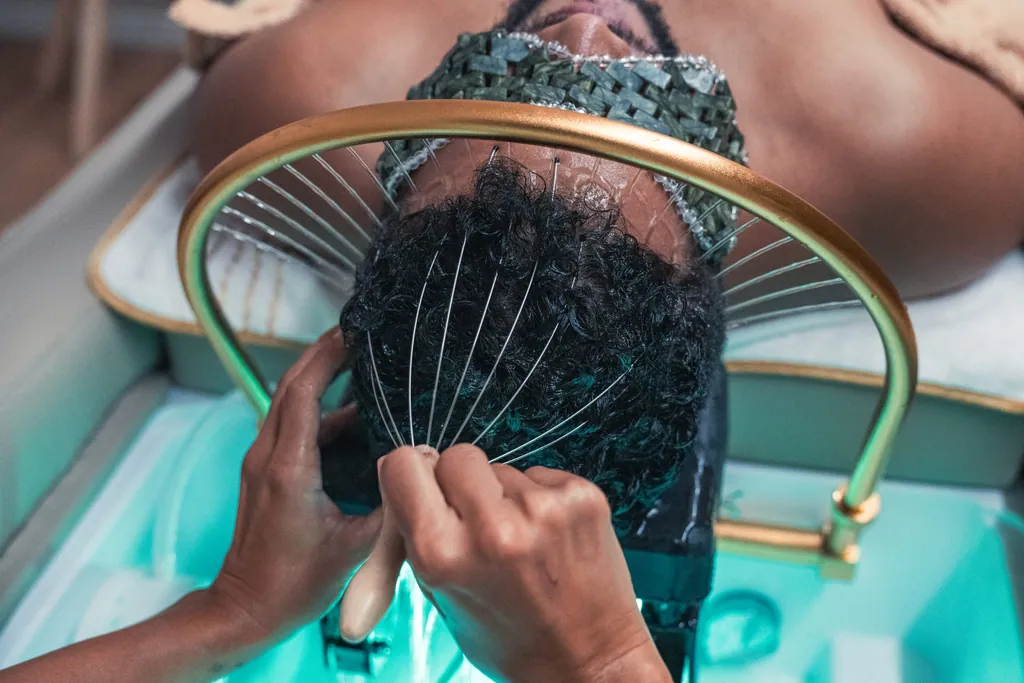 Terapeuta a passar um massajador pelo cabelo de uma pessoa, sob o arco dourado do Head Spa