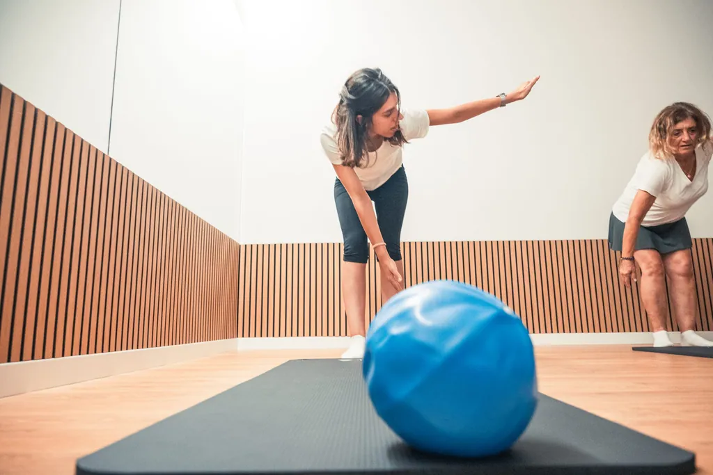 Instrutora a demonstrar um exercício de pilates a uma aluna, com uma bola azul sobre o tapete